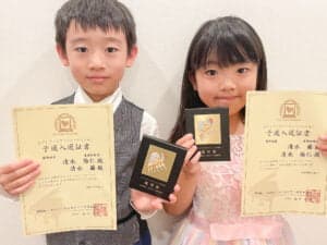 賞状とトロフィーを持つ男の子と女の子